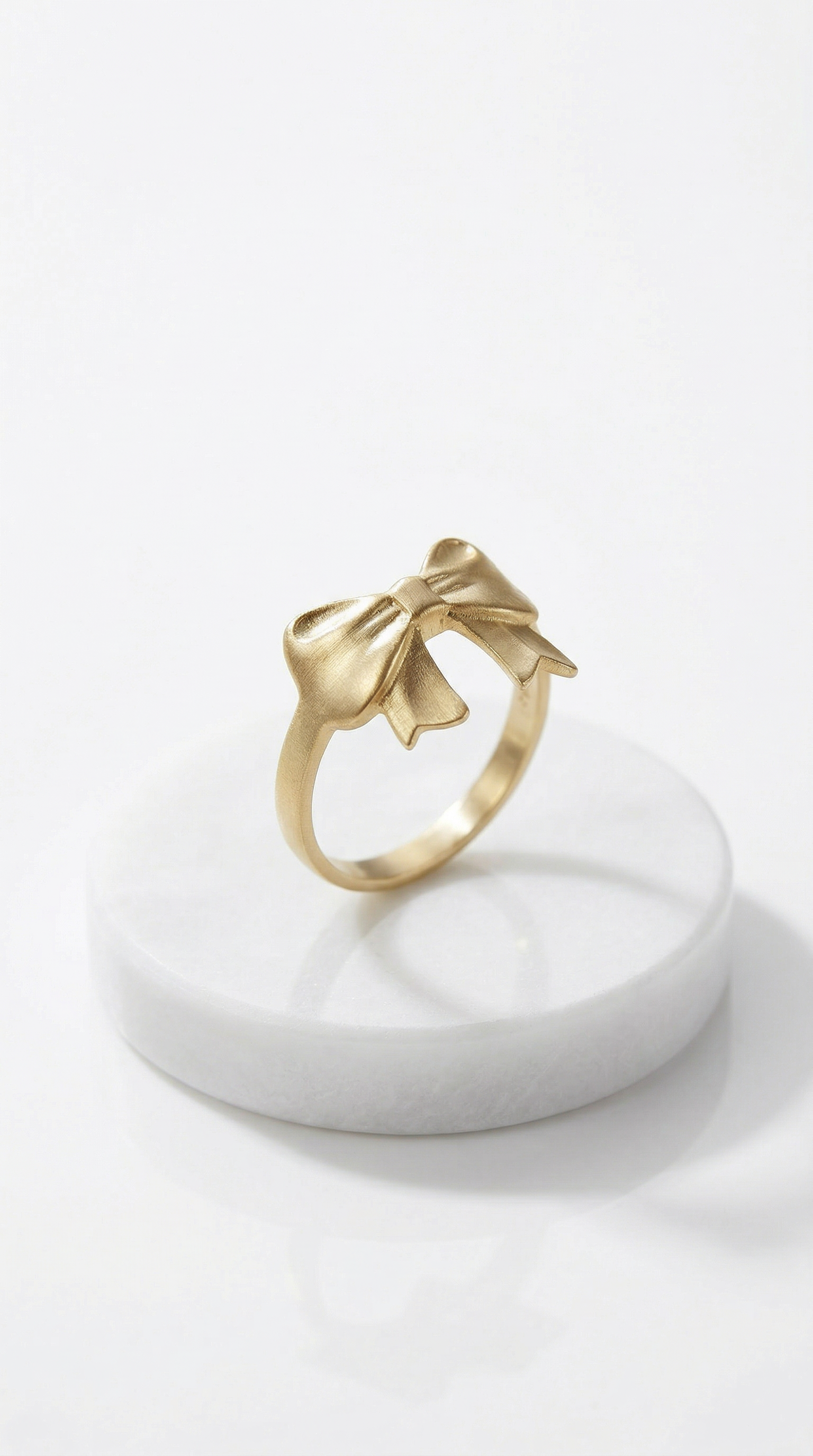 Gold ring with bow design on a white marble stand