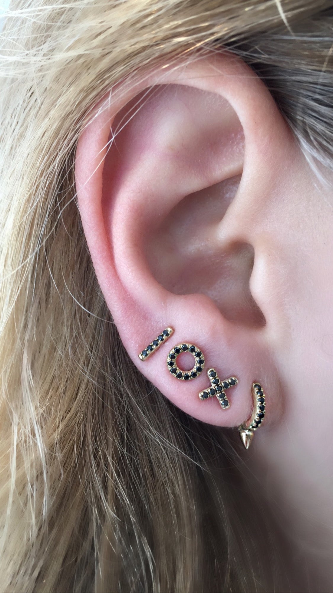 Close-up of an ear wearing two gold earrings with gemstones.